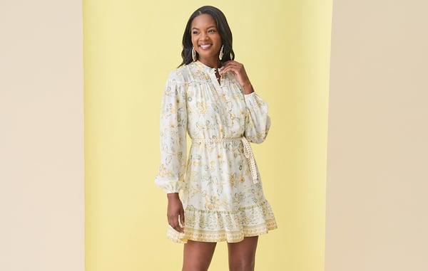 Women is wearing a yellow and white floral mini dress while posing in front of a yellow background.