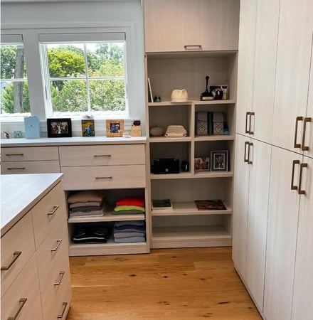 Light toned walk-in closet with center island and dresser under window.