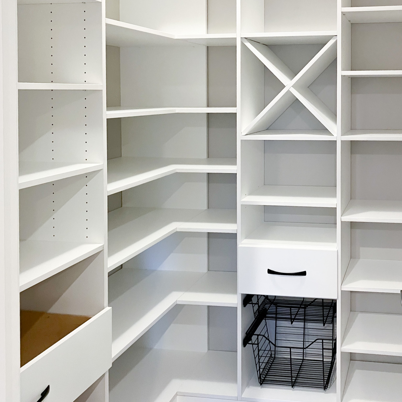 White pantry with open shelving, wine storage, wide set drawers, and metal basket.