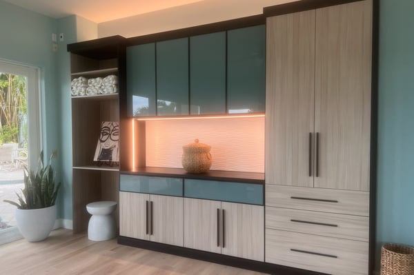 Custom home gym with wet bar capabilities in Cassini Beach and Shadow Black finishes, matte black hardware, black in-surface power station, Onyx aluminum frame doors and drawers with lagoon gloss back-painted glass, and integrated vertical, under-cabinet, and up lighting.