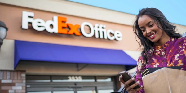 Student holding phone and packages in front of FedEx Office