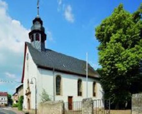 Außenansicht der weißen Kirche mit schwarzem Dach vor blauem Himmel.