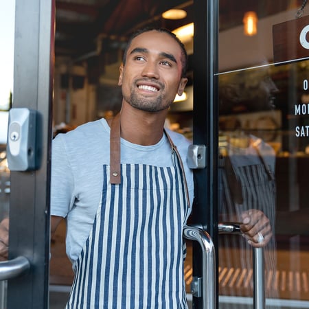 A man in an apron opening a business door