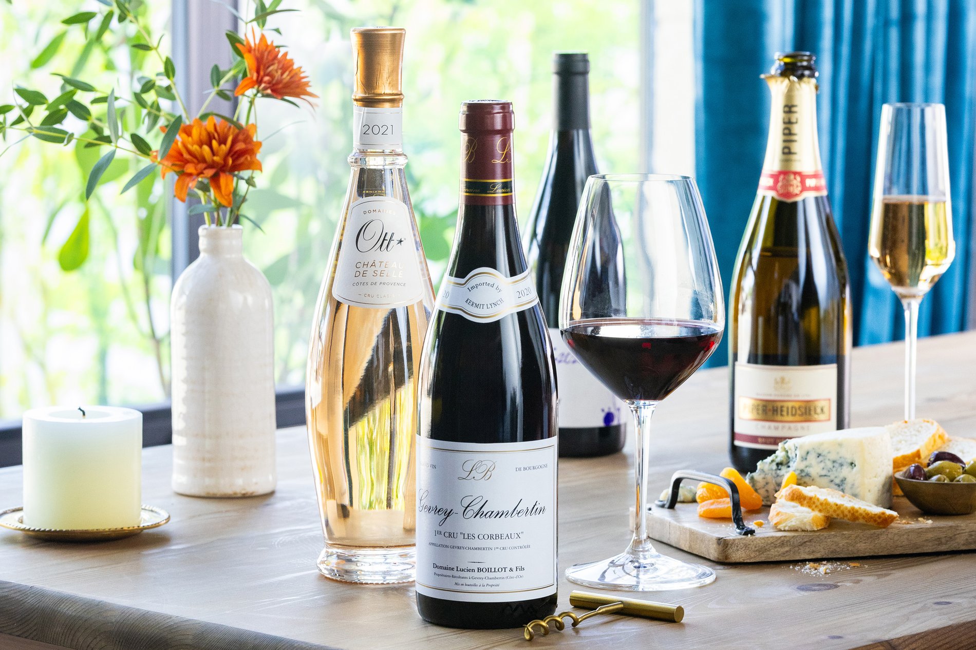 assorted red and sparkling wine bottles with a wine glass and appetizers on a table styled for a celebration or party