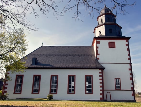 Die weiße Außenfassade der Kirche mit Schieferdach bei schönem Wetter.