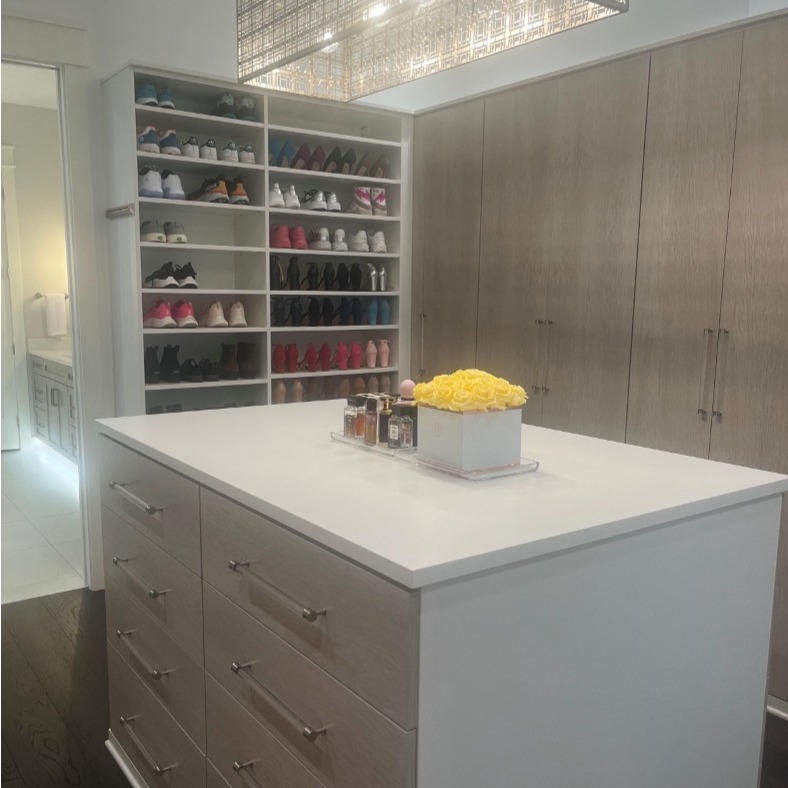 Custom walk-in wardrobe style closet with island in Morning Mist finish and Adriatic Mist drawers and doors, featuring custom acrylic hardware and full-door design to keep garments concealed.