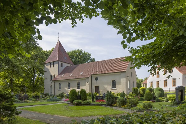 Das Kirchengebäuden mit Friedhof, umringt von Bäumen.