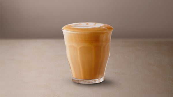 A Cortado in a glass placed on a beige surface.