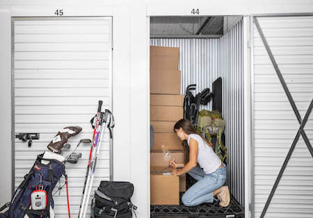 Woman labels boxes in her storage unit containing camping gear, skiis, golf clubs, boxes and more