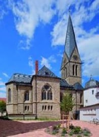 Außenansicht der Kirche im neugotischen Stil vor blauem Himmel. Herausragend ist der spitze Kirchturm.