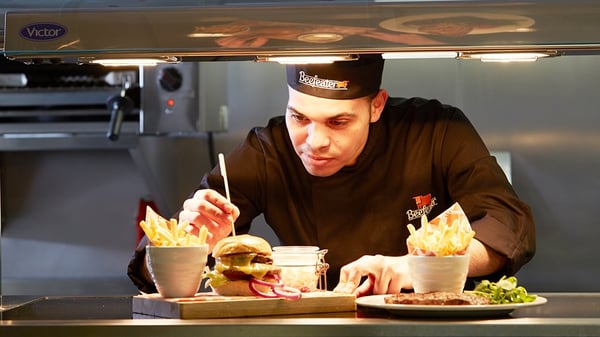 A Whitbread employee prepares a customers order, a burger and fries at the window.