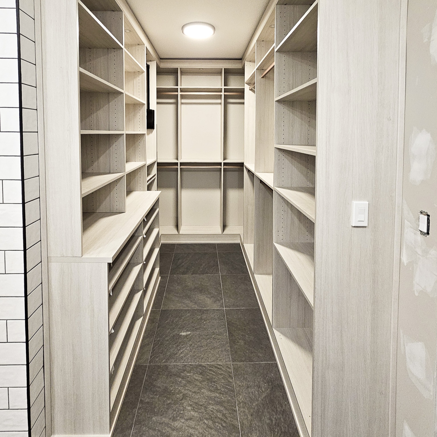 Narrow walk in closet maximized with floor to ceiling storage. Designed in a light wood grain finish with open shelving double hang.