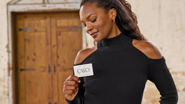Woman is wearing a black sweater and holding up a Cato Fashions gift card.