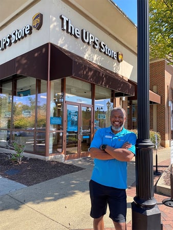 Smiling man in sky blue shirt standing outside, in front of The UPS Store