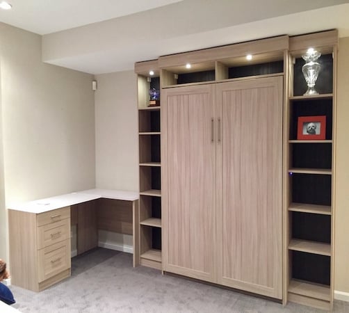 Murphy bed with desk, shelves, and cabinets in light wood by California Closets Northern Michigan