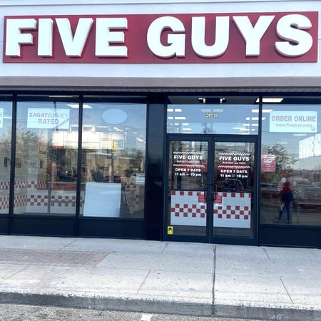 Exterior photograph of the entrance to the Five Guys restaurant at 70 Atlantic Avenue in Oceanside, New York.