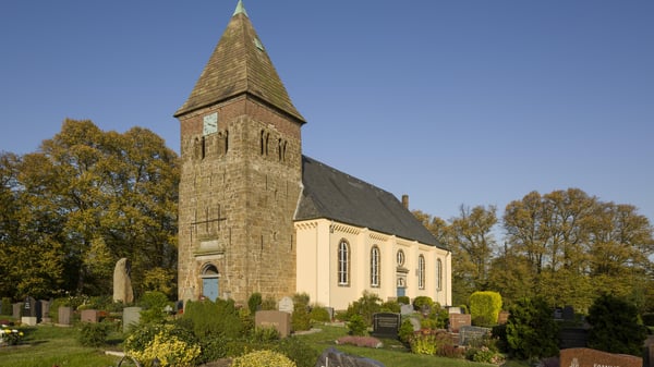 Das Kirchengebäude umringt von einem Friedhof und Bäumen.