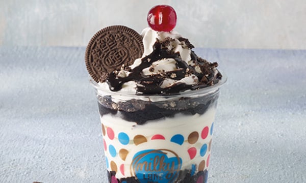 Ice cream sundae with swirled ice cream, chocolate sauce a cherry and an OREO® cookie in a transparent plastic cup