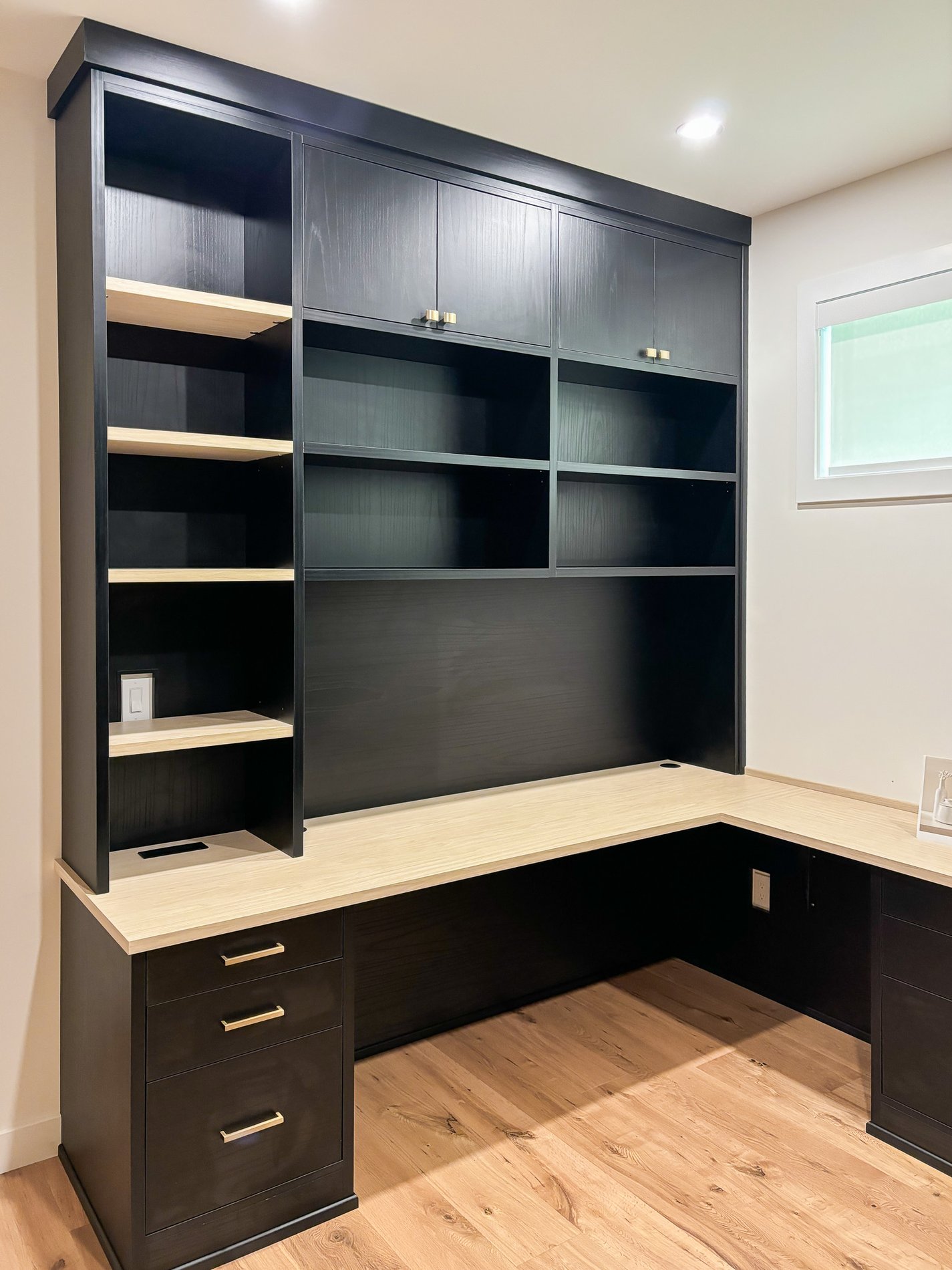 A black and modern home office space with light accent finishes, gold hardware and plenty of storage for office supplies.