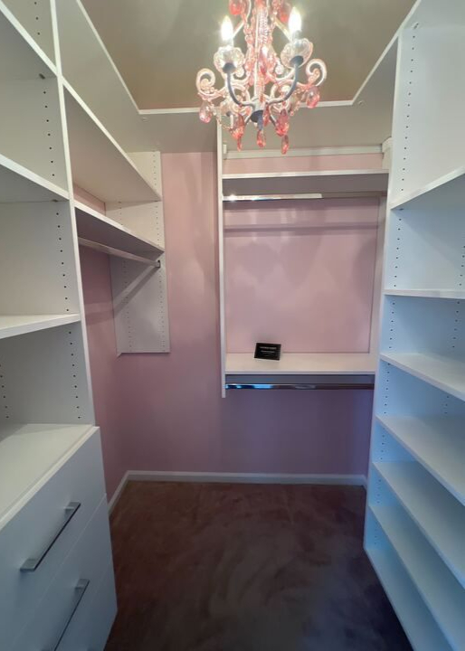 Virginia Beach - Custom closets - Walk-in closet with white shelving and pink walls under chandelier lighting.