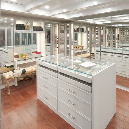 White walk in closet with mirrored doors, a vanity, and center island.