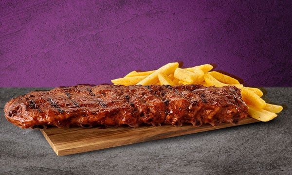 A single rack of loin pork ribs with a side portion of chips on a wooden board placed on a grey surface with a grey background.