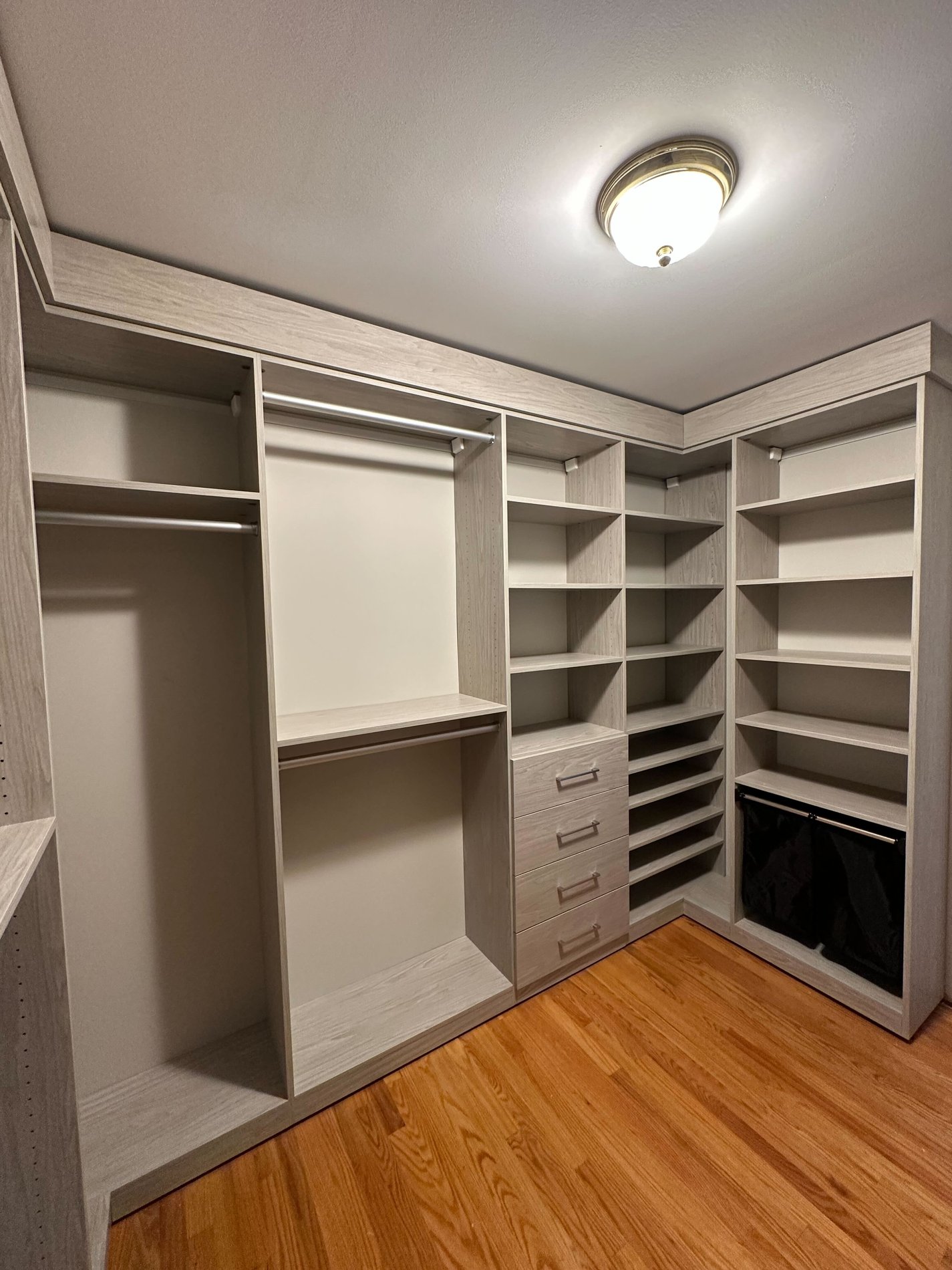 Walk-in closet in a light wood finish with hanging space, shelving, drawers and pull-out hamper.