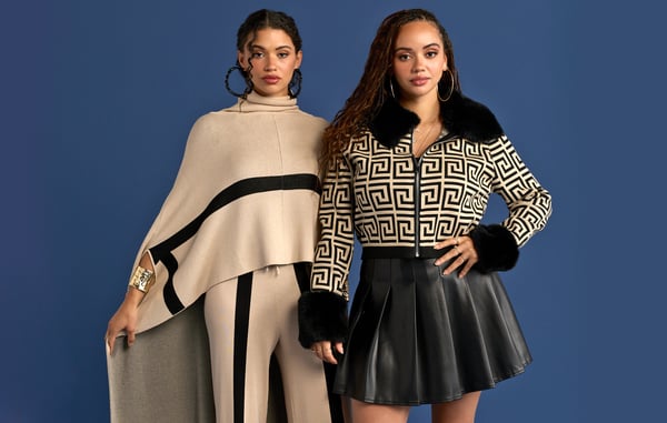 Two women are wearing fall outfits and posing in front of a blue wall.