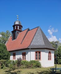 Außenansicht der Kirche bei blauem Himmel. Die Kirche ist umgeben von einer Grünfläche.