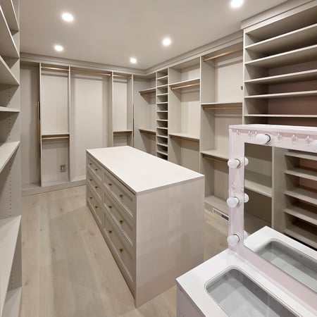 Walk in closet with floor to ceiling storage and a centre island. Designed in a light off white finish with gold hardware.