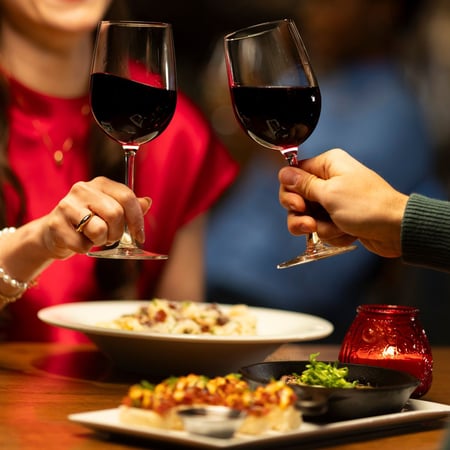 A cheers over dinner plates with two red wine glasses