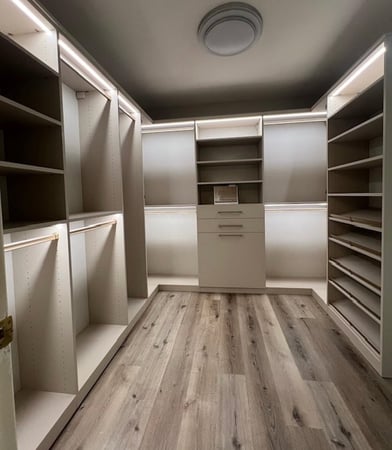 Custom primary closet in linen and stone with gold elite handles and strip lighting.