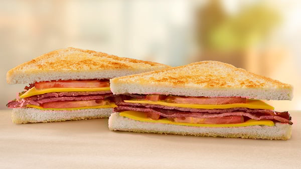 A Macon, Cheese & Tomato Toasted Sandwich on a brown surface with a blurred background.