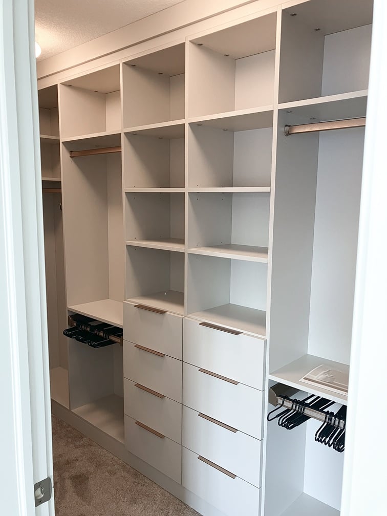 Simple walk in closets in an off white finish with drawers, shelving, and hanging.