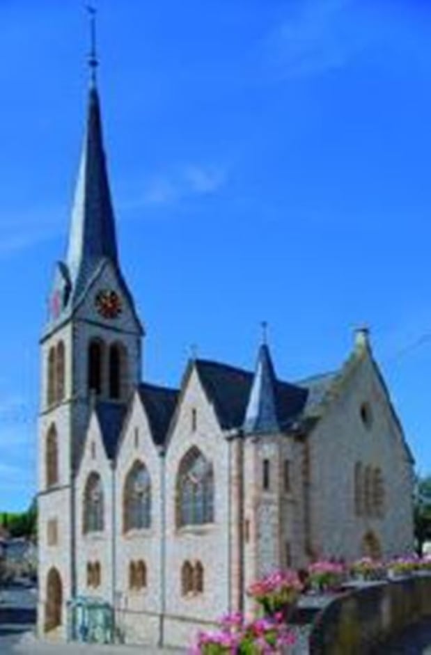 Außenansicht der Kirche vor blauem Himmel. Der Kirchturm ragt besonders heraus.