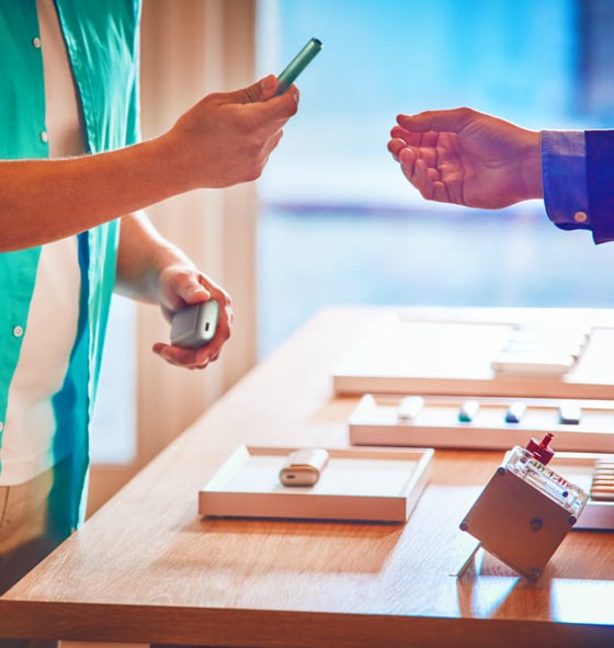 In a IQOS Store there is a man holding an IQOS ILUMA holder and an IQOS Expert