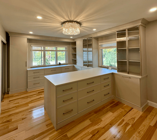 luxury, custom walk-in closet for her with light wood, large peninsula and glass doors