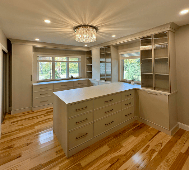 luxury, custom walk-in closet for her with light wood, large peninsula and glass doors