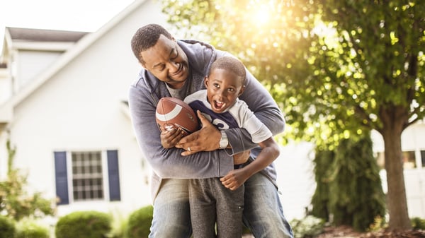 A man 
laughs as he holds a young child with a football