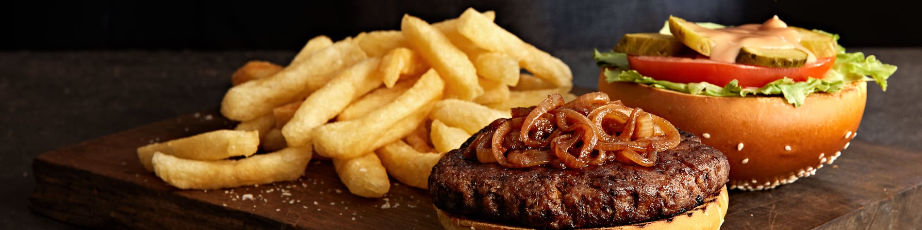 Beef burger and chips on a wooden board against a grey background.