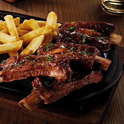 Sliced rack of ribs next to salted potato chips on a wooden board