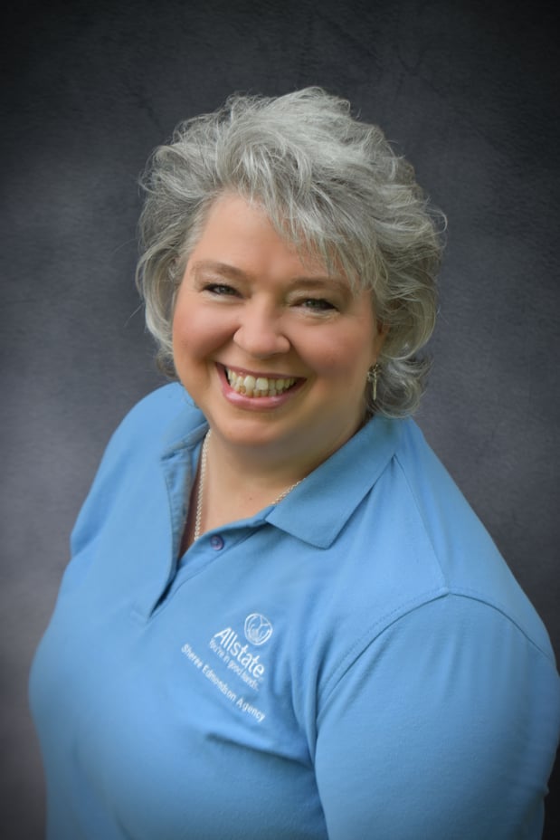 Smiling woman with short, silver hair wearing a light blue Allstate polo shirt embroidered with “Sheree Edmondson Agency,” posed against a dark gray backdrop.