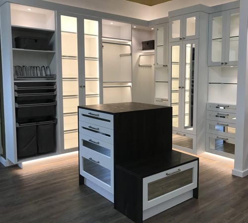 Large, white walk-in closet with recessed lighting and glass shelves