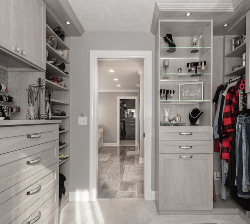 Light grey walk-in closet with hanging space, shelving, drawers, and cabinets.
