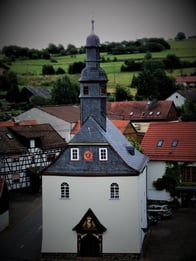 Fachwerkkirche, 1698 erbaut, Portal mit Wappen, mitelalterliches Kruzifix über dem Altar, bäuerliche Barockmalerei an den Emporenbrüstungen.