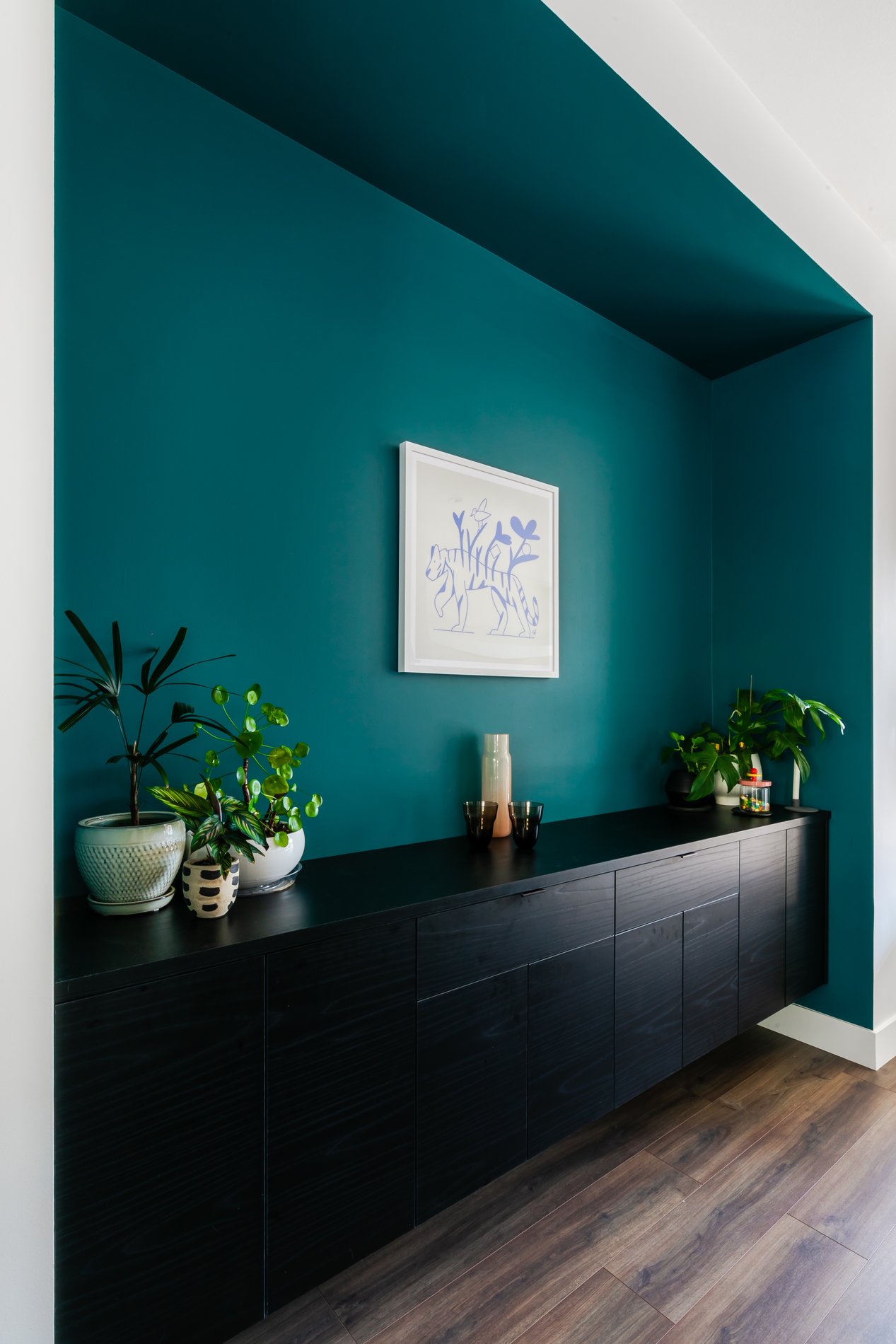 Painted green nook with black cabinets and plants on top.