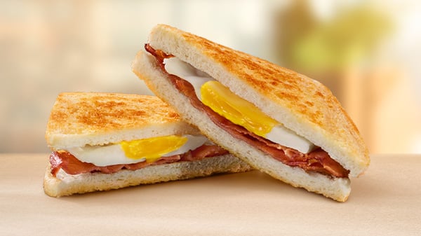 A Bacon & Egg Toasted Sandwich on a brown surface with a blurred background.