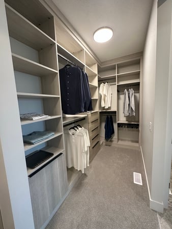Walk-in closet with with shelving, double hanging, drawers and pull out laundry basket. Designed in a light wood gray wood grain finish with black hardware.