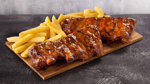 Two racks of beef ribs with a portion of hand-cut chips on a granite surface.