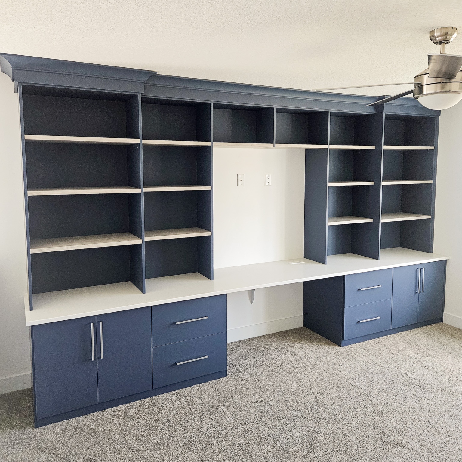Home office in a deep blue matte finish with white shelves and traditional crown molding.
